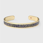Close-up of SWAROVSKI® Heliotrope crystal fabric inlay on gold cuff, showing violet-blue sparkle and precision-cut texture.